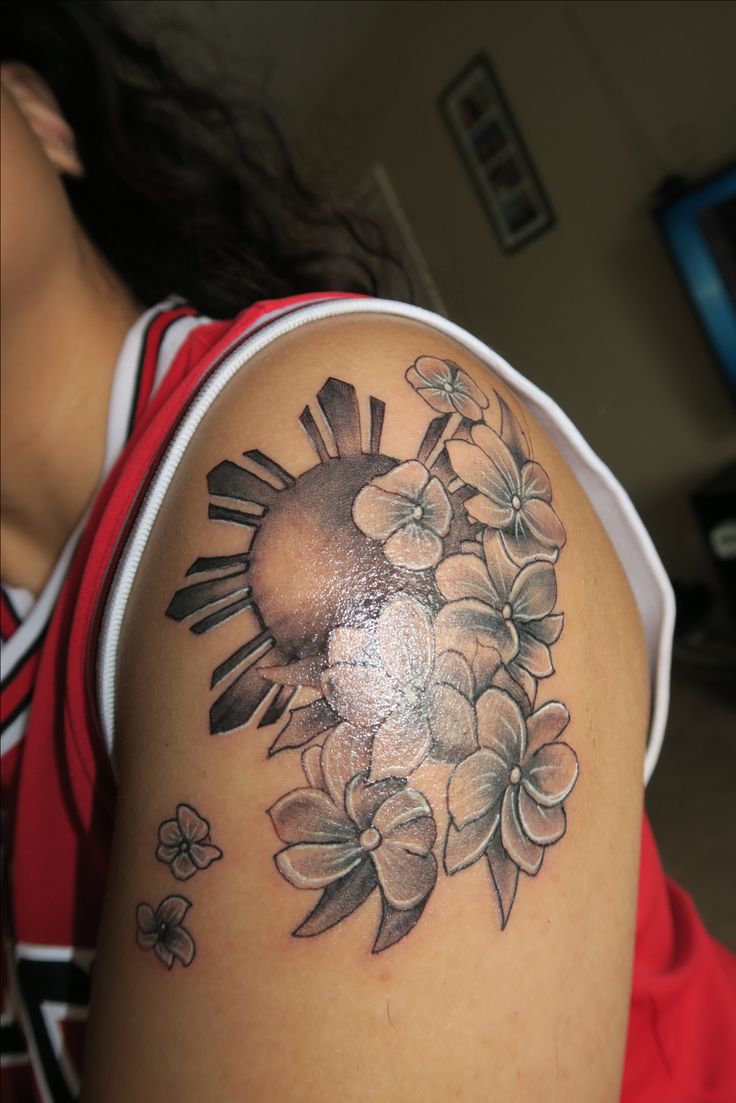 a woman's arm with flowers and a sun tattoo on her left side shoulder