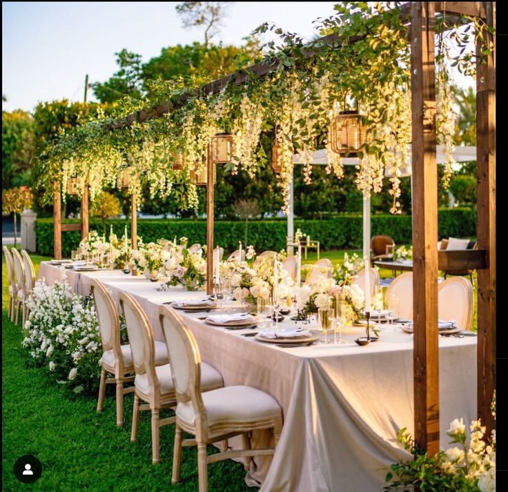 a long table set up with white flowers and greenery for an outdoor wedding reception