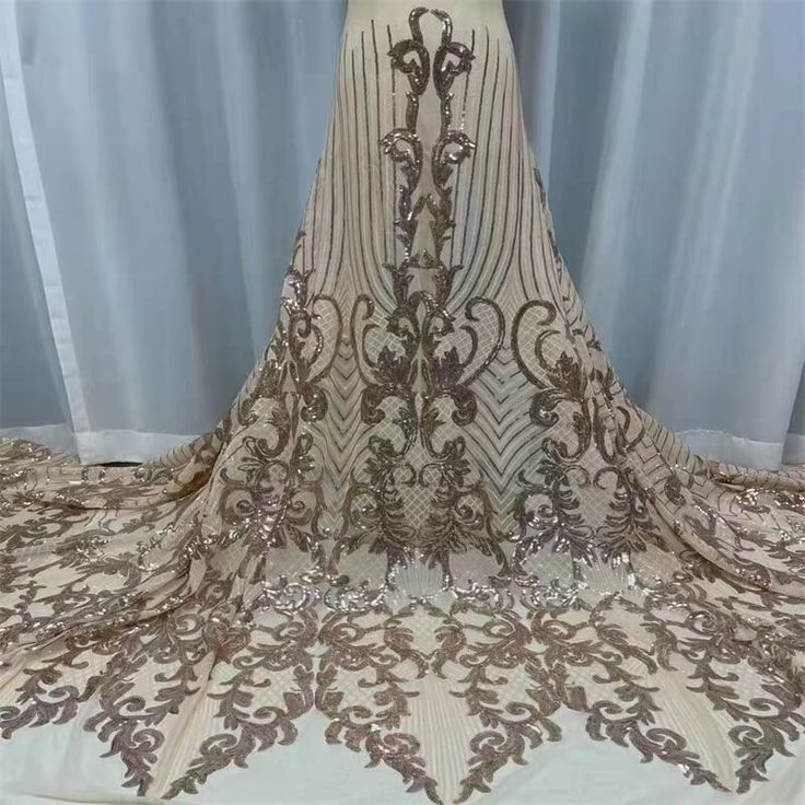 a dress is shown on display in front of a curtain with an intricate lace pattern