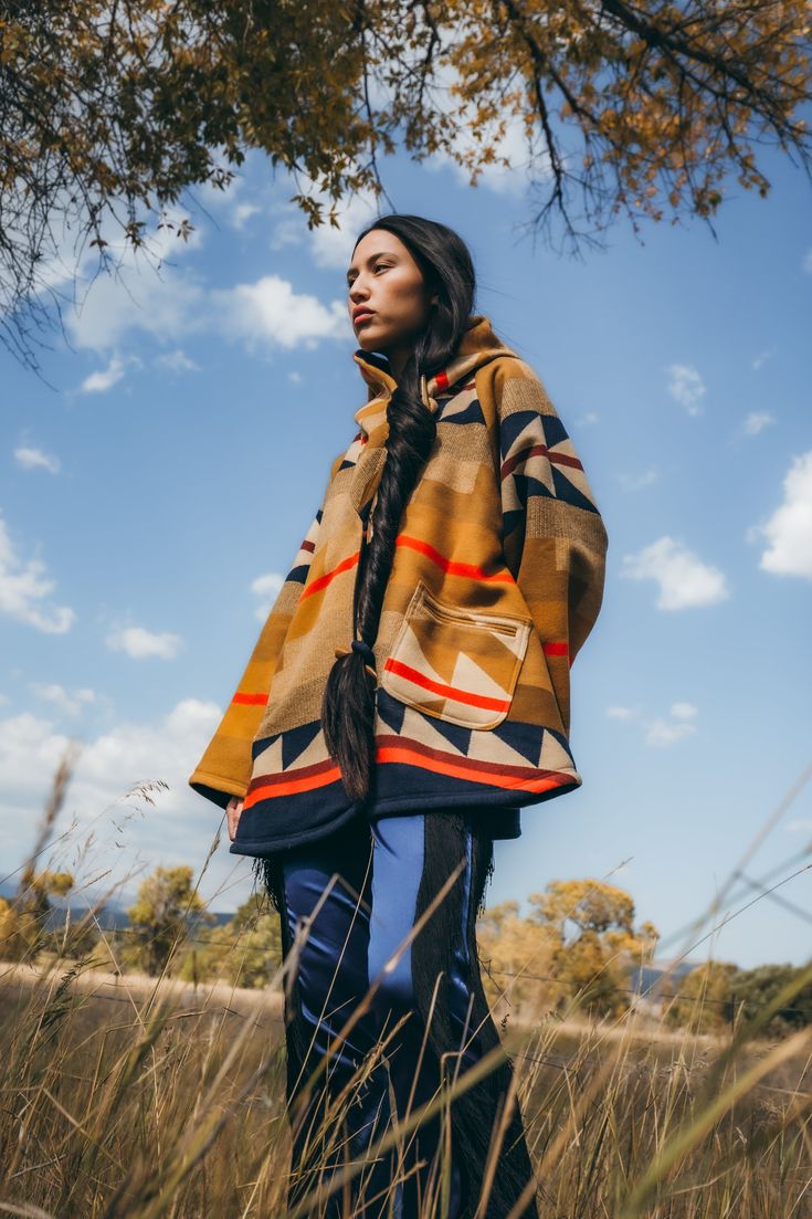 Bell-shaped hooded cloak with welt patch pockets and 3 toggle closure. Corine is 5'9" and wears size OS. Unnapped Pendleton blankets: 82% Wool, 18% Cotton. Wool Cashmere facings and Silk Rayon peachskin lining. Native American tribes traveled to Wyoming’s Medicine Bow Mountains to harvest wood for especially fine bows. In this design, stands of wood alternate with arrows that meet in the center to evoke the Medicine Bow River, an important crossing point through the Continental Divide. Expertly Hooded Fall Poncho With Pockets, Fall Hooded Poncho With Pockets, Hooded Poncho With Pockets For Fall, Pendleton Blankets, Pendleton Blanket, Continental Divide, Classic Blouses, Sweat Dress, Hooded Cloak