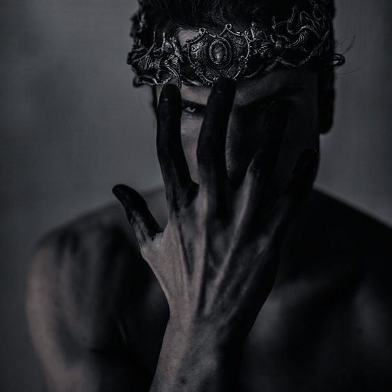 a black and white photo of a man with his hands on his face wearing a crown