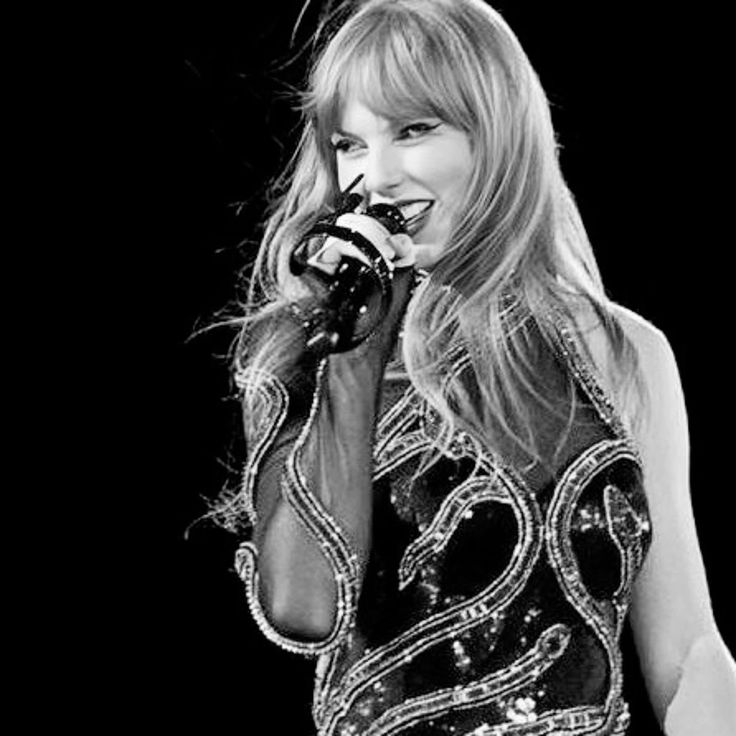 a woman in a black and white dress holding a microphone up to her mouth while standing on stage