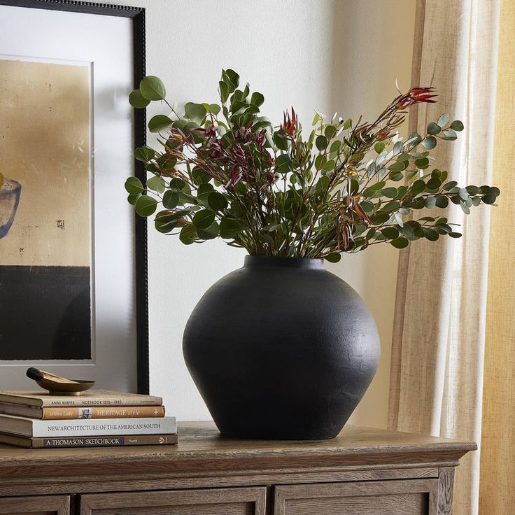 a black vase sitting on top of a wooden table next to a framed photo and books