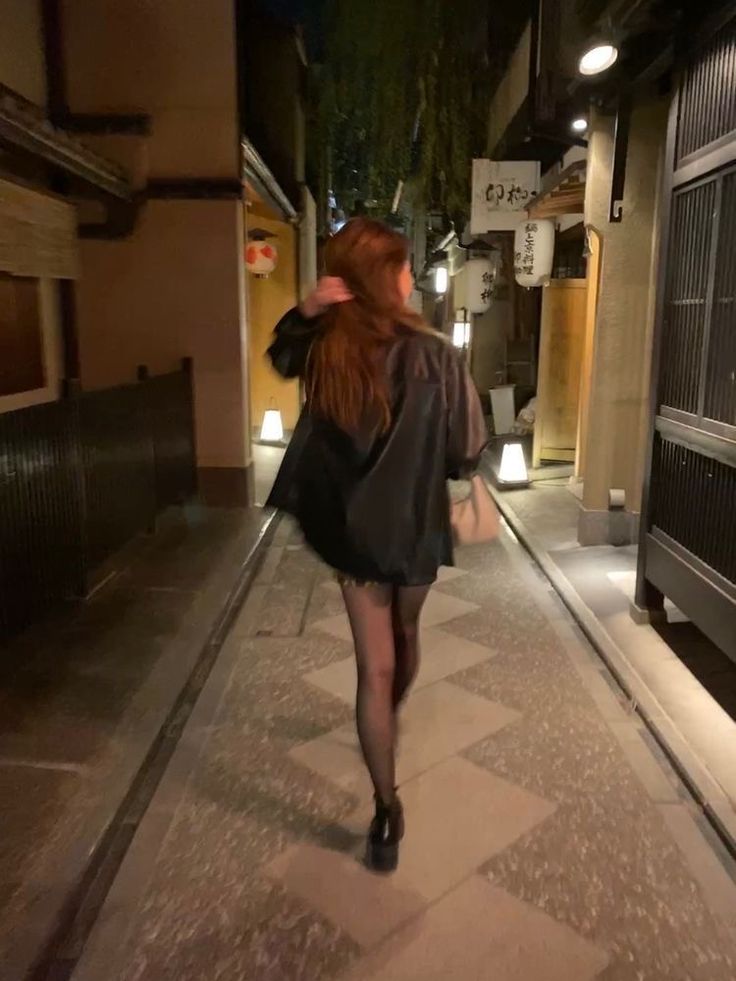 a woman is walking down the street at night with her back turned to the camera