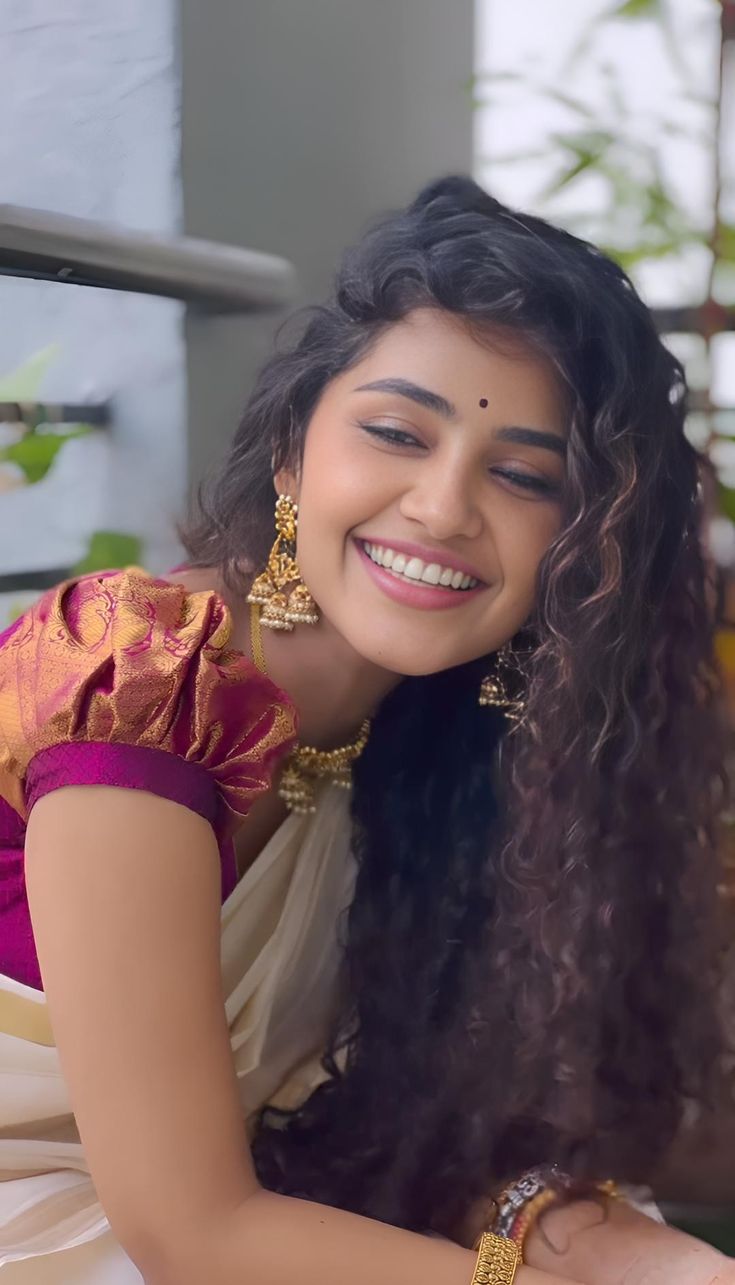 a woman with long black hair wearing a yellow and pink sari smiling at the camera