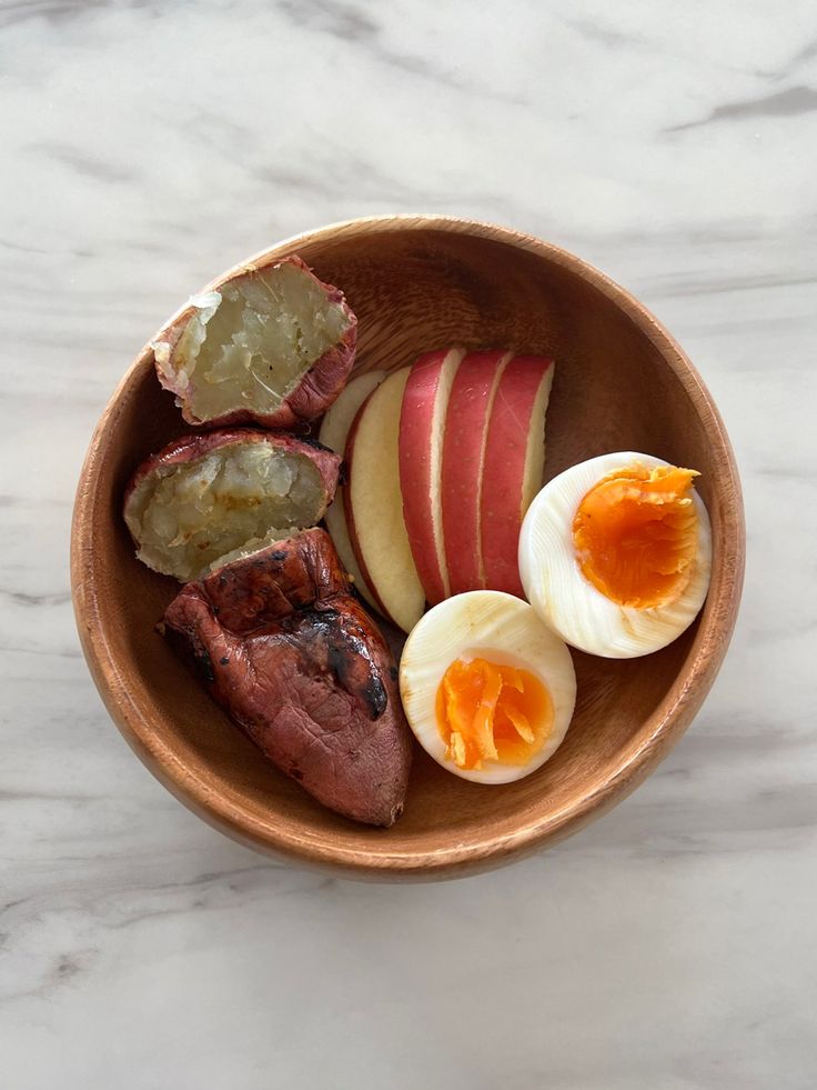 a wooden bowl filled with meat, an egg and sliced up apples on top of a white marble counter