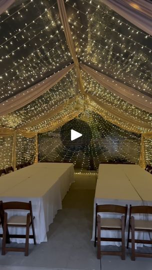 the inside of a large tent with tables and chairs under string lights on the ceiling