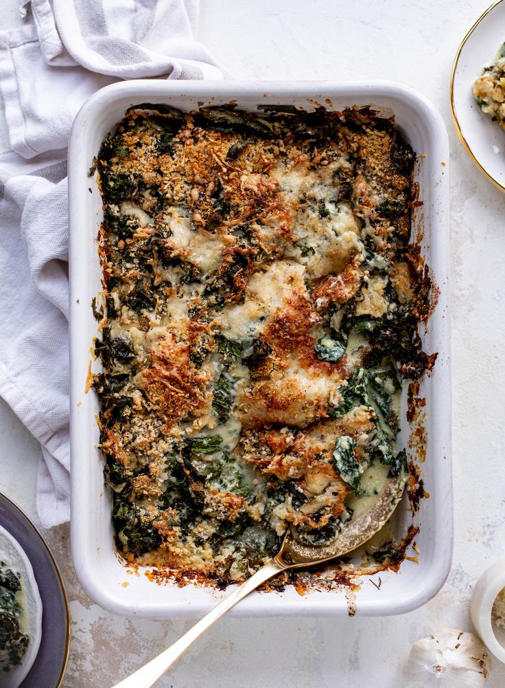 a casserole dish with spinach, cheese and bread crumbs on the side