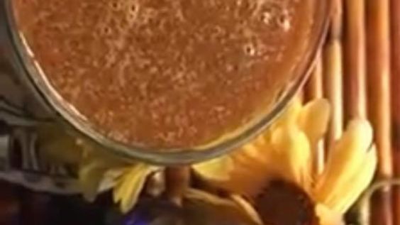 a glass filled with liquid sitting on top of a table next to bananas and flowers