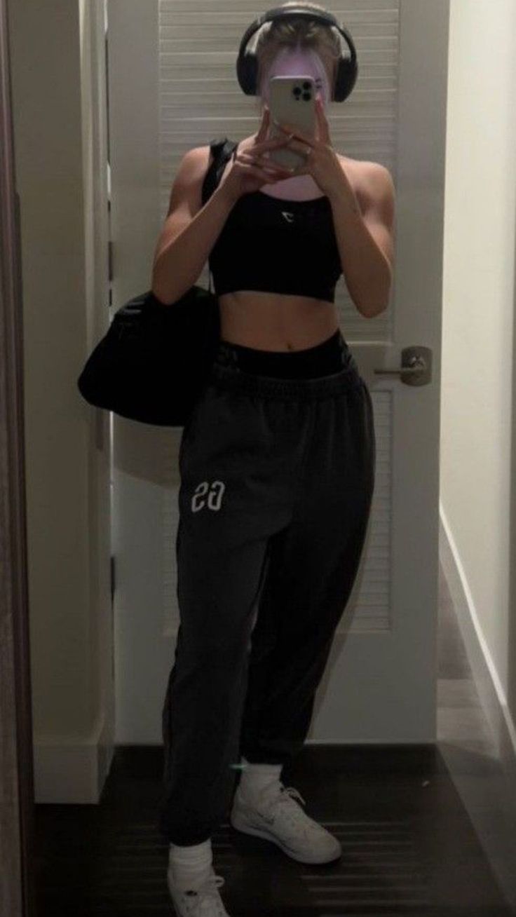 a woman taking a selfie in front of a mirror wearing headphones and black sweatpants