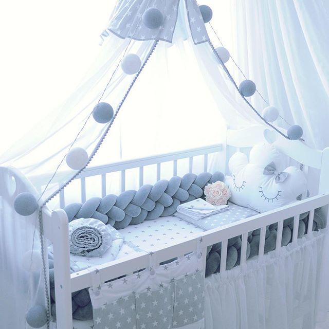 a baby crib with white curtains and grey balls on it, in the middle of a room