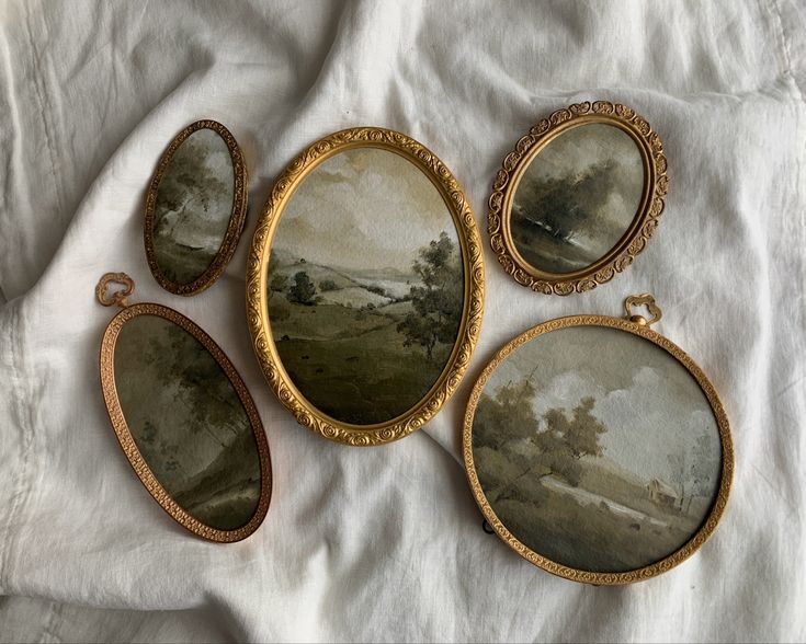 three oval paintings are sitting on a white sheet next to an open pocket watch and keychain