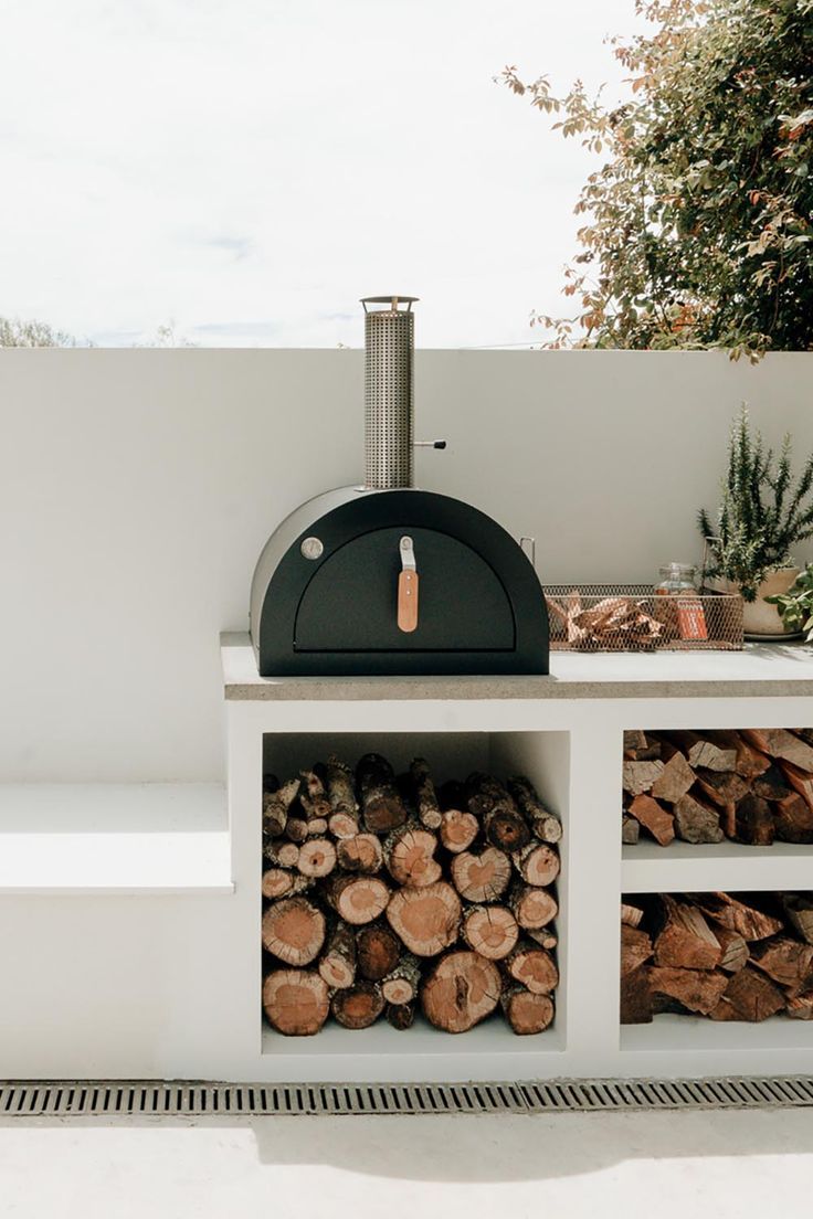 a pizza oven sitting on top of a white counter next to logs and pine trees