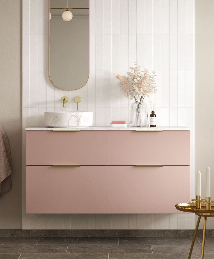 a bathroom with pink cabinets and gold accents on the countertop, along with a mirror