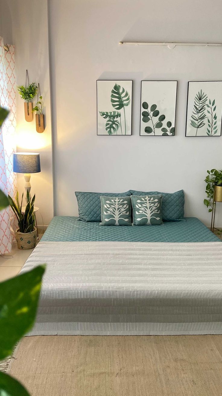 a bed sitting in a bedroom next to two plant wall hanging on the wall above it