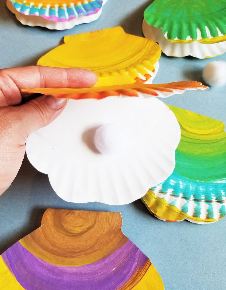 a person holding a plastic toothbrush in front of some colorful paper seashells