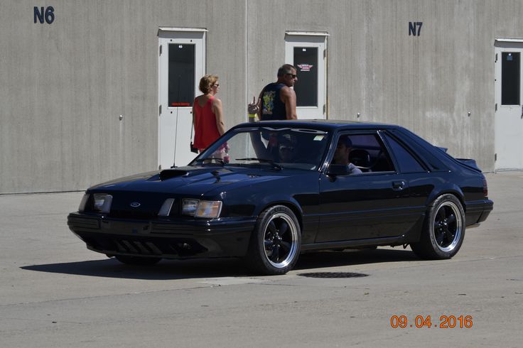 a black car parked in front of a building with two people standing around looking at it