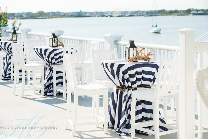 there are many chairs and tables set up on the deck by the water with blue and white striped cloths