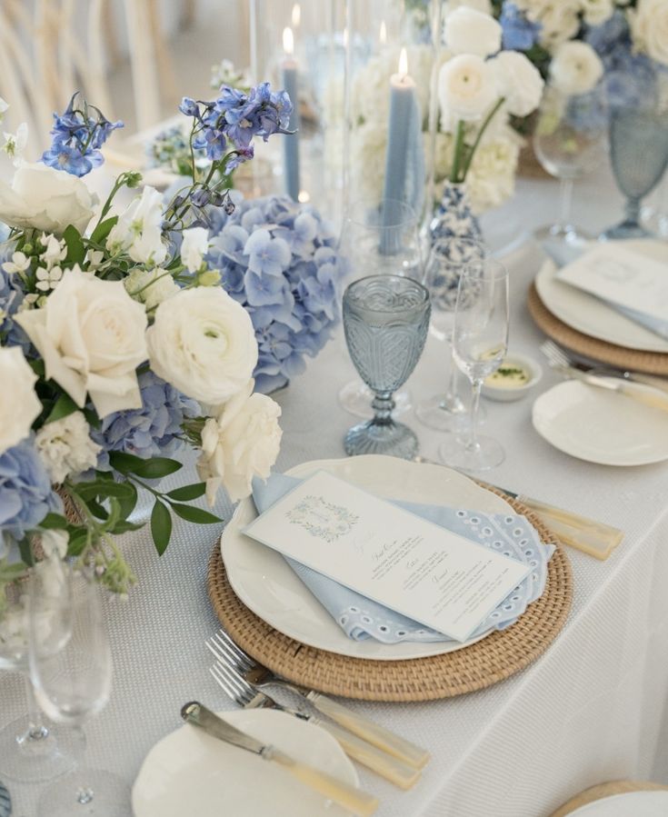 the table is set with blue and white flowers, silverware, and napkins