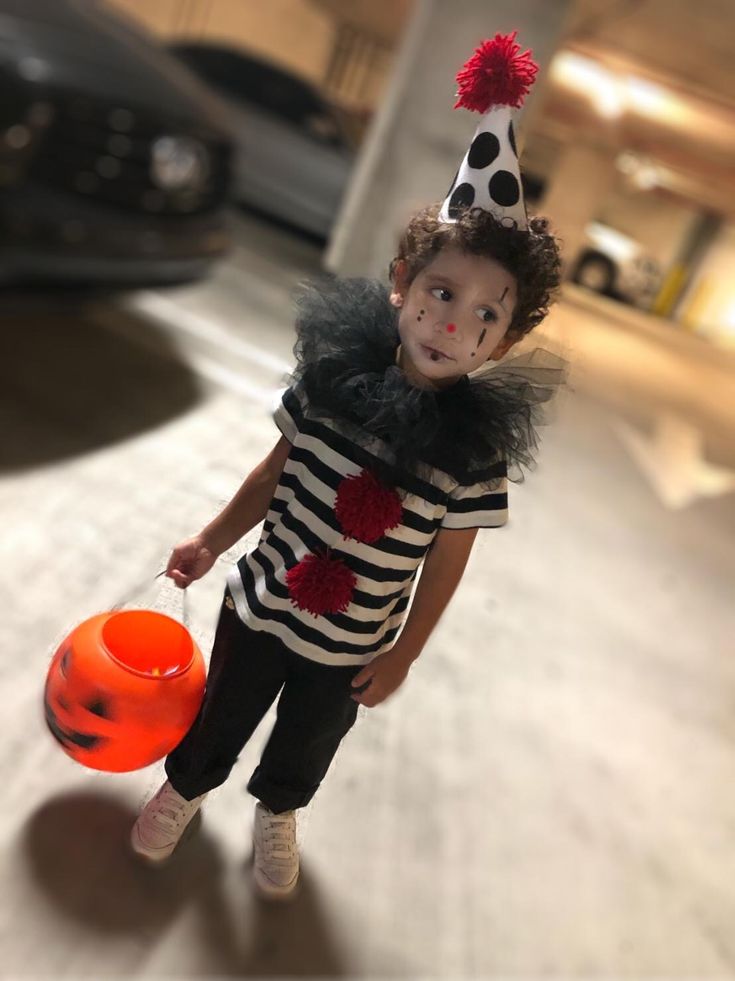 a young boy dressed up as a clown holding an orange frisbee