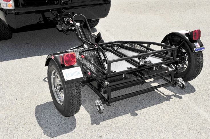 a motorcycle trailer attached to the back of a car in a parking lot with another vehicle behind it