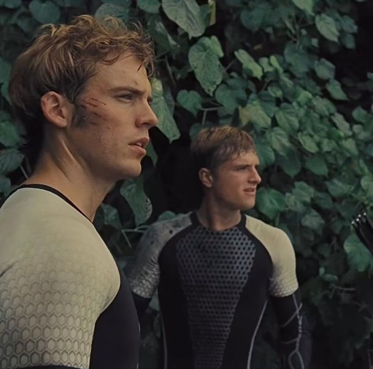 two men standing next to each other in front of plants