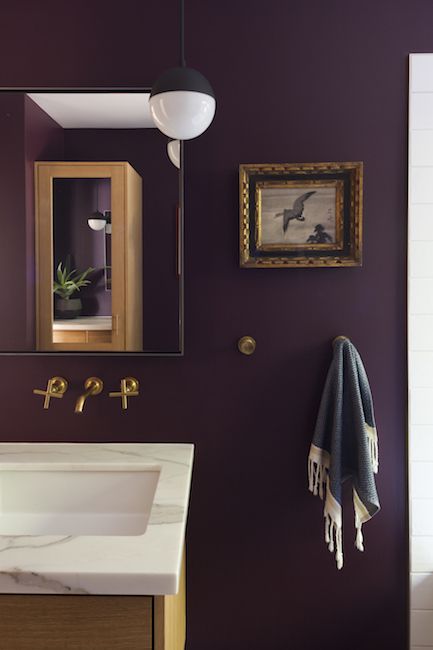 a bathroom with purple walls and white counter tops, gold accents on the mirror above the sink