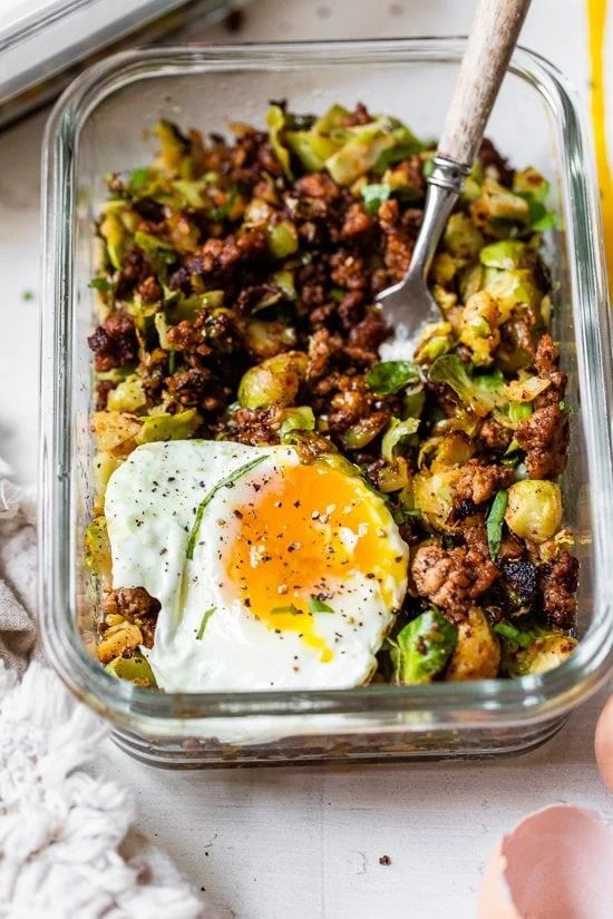 a glass dish filled with meat, vegetables and an egg on top of the food