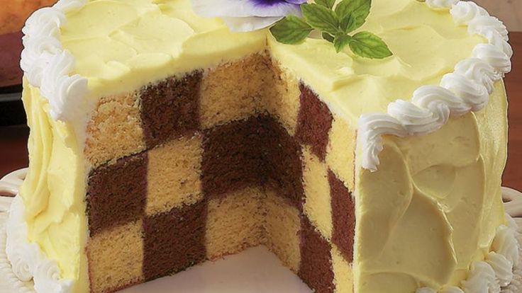 a cake with white frosting and brown checkerboard design on the inside is cut in half