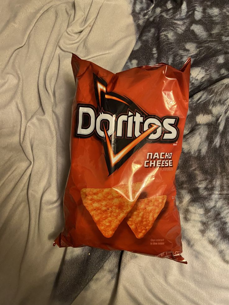 a bag of doritos chips sitting on top of a white bed sheet next to a pillow