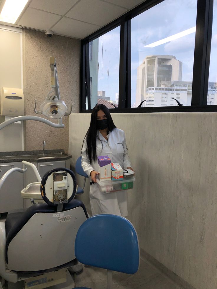 a woman standing next to a dental chair in a room with large windows and medical equipment