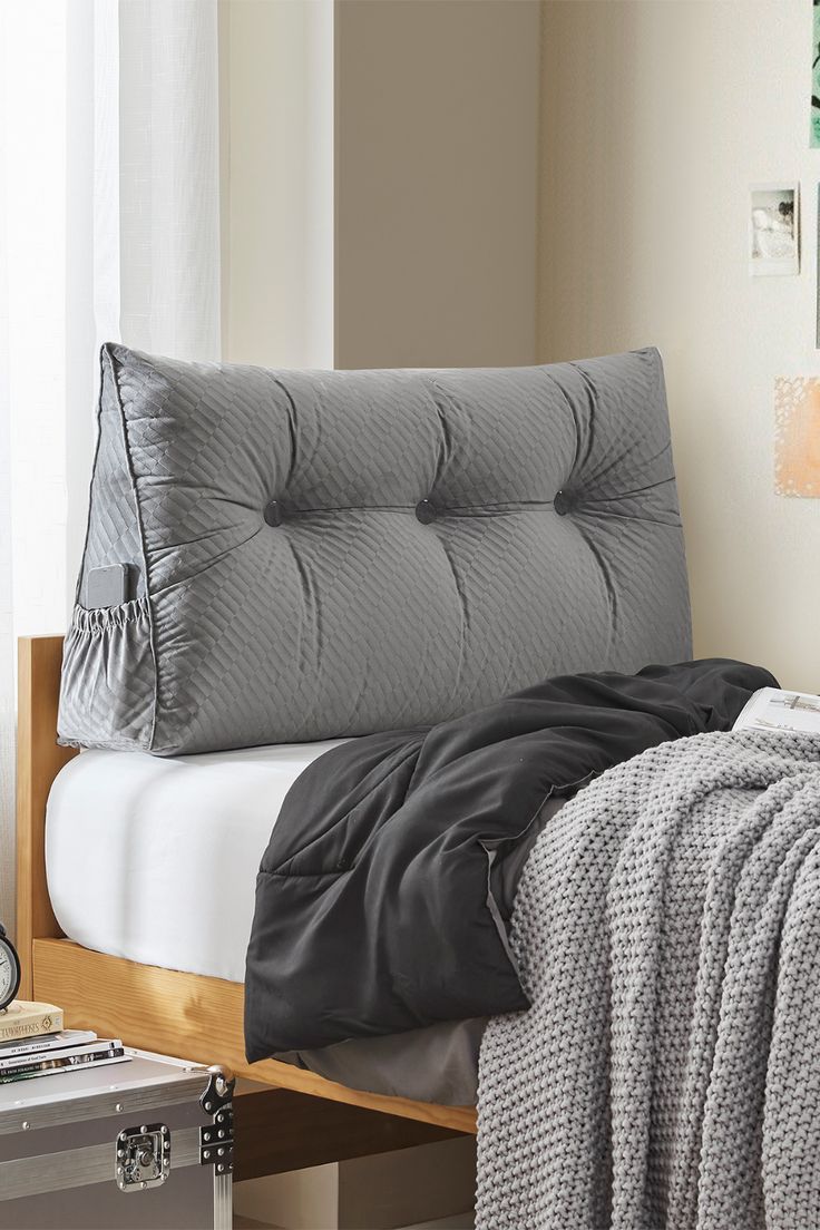 a bed with a gray comforter on top of it next to a white wall