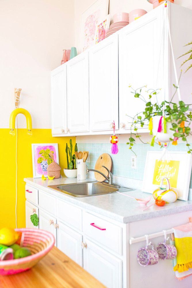 a kitchen with yellow walls and white cabinets, wooden counter tops and colorful artwork on the wall