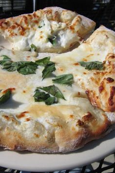 two slices of pizza with cheese and basil on a white plate sitting on a table