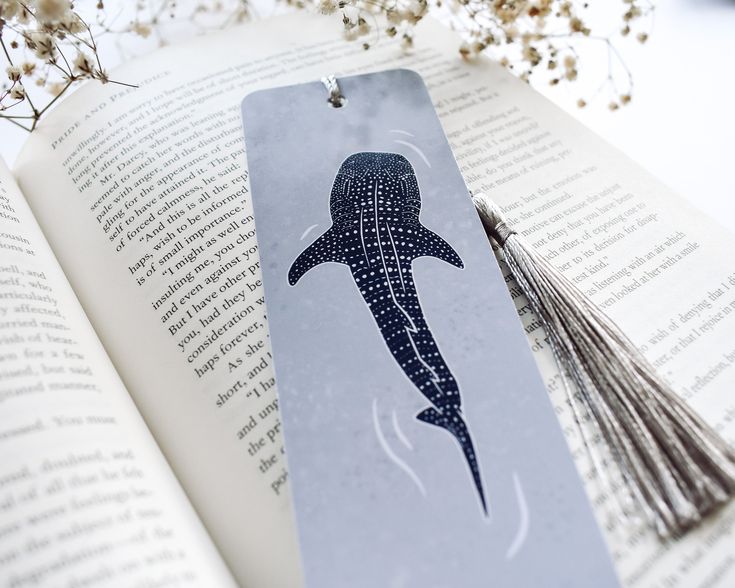 a bookmark with a whale drawn on it and tassels attached to it