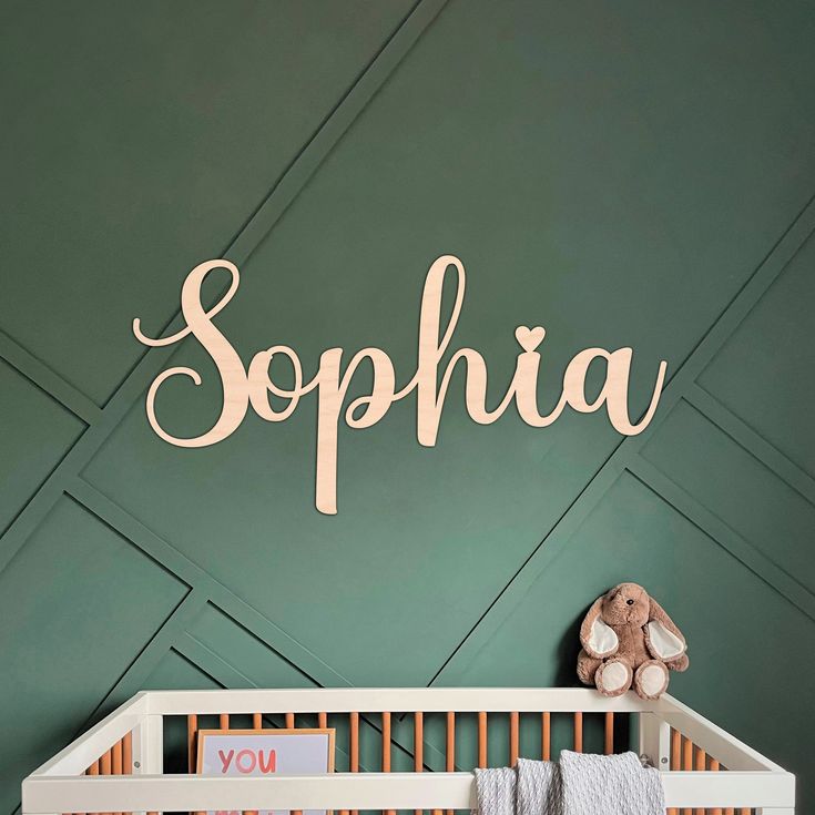 a baby's room with green walls and white crib, teddy bear and name sign