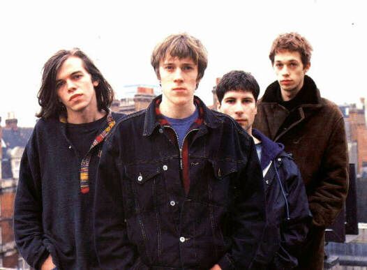 four young men standing next to each other in front of a cityscape with tall buildings