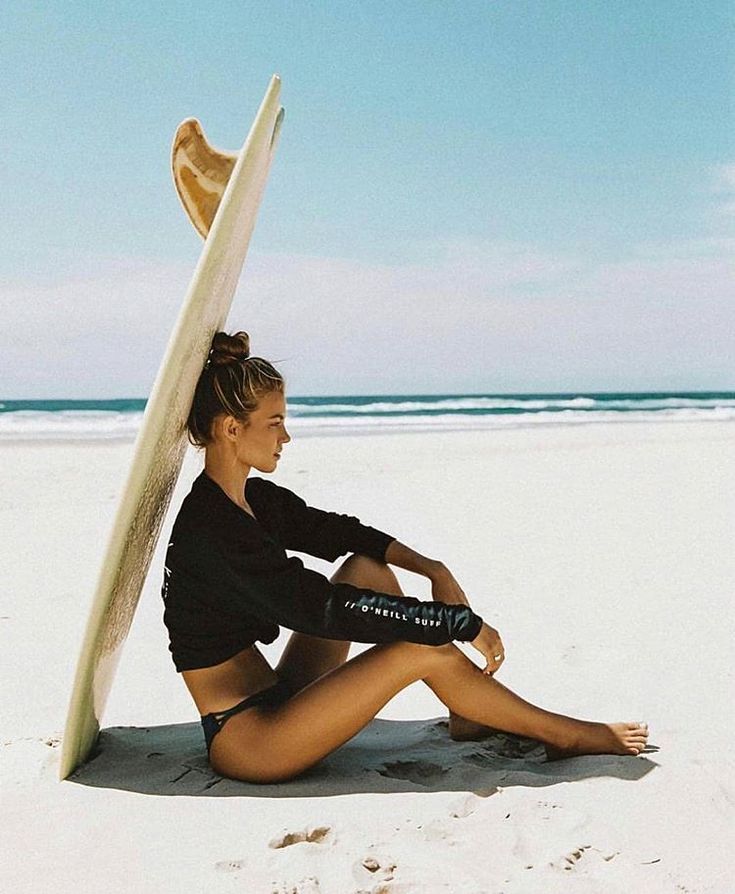 a woman sitting on the beach with her surfboard