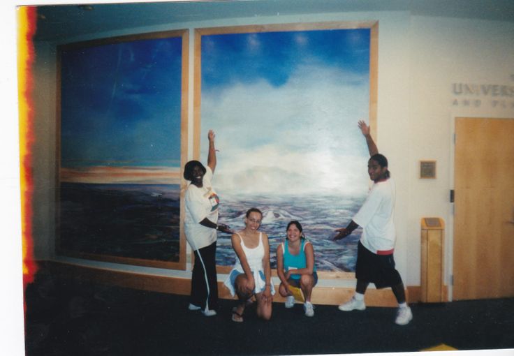 three people are standing in front of a painting on the wall with their arms up