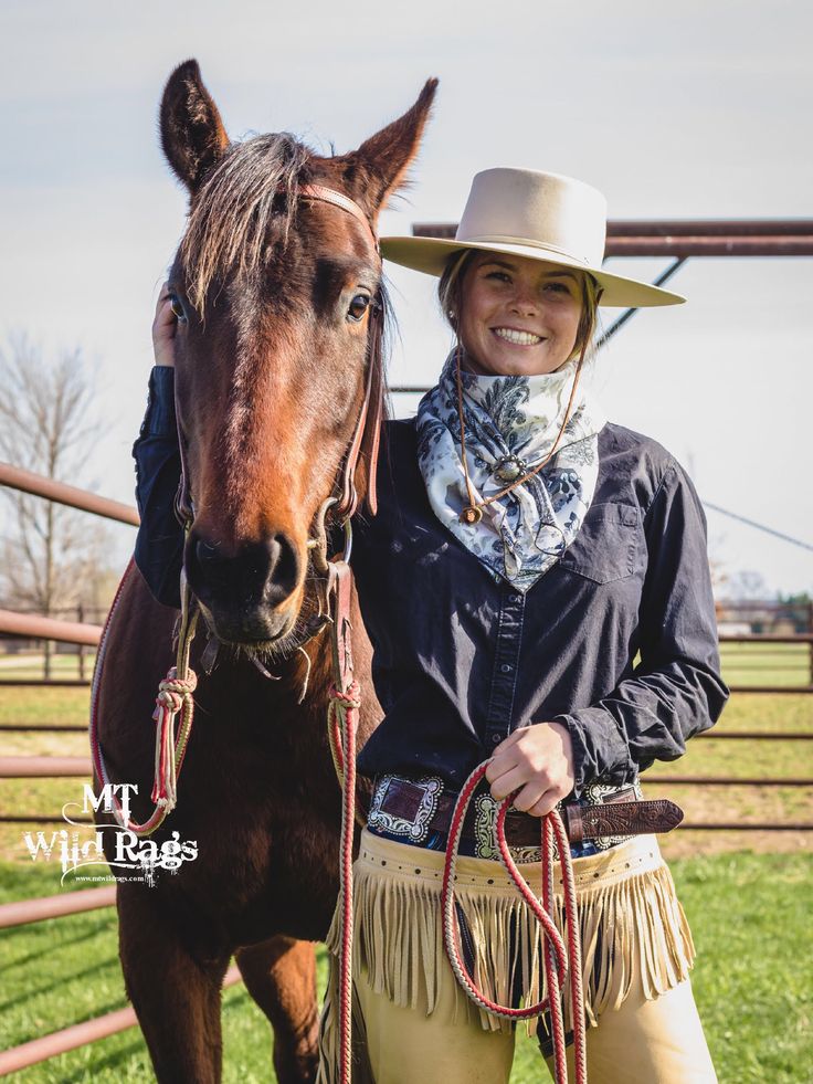 a woman standing next to a brown horse wearing a cowboy hat and holding the reins