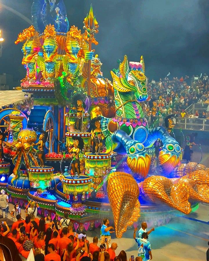 an elaborately decorated float in the middle of a carnival parade at night with lots of people watching