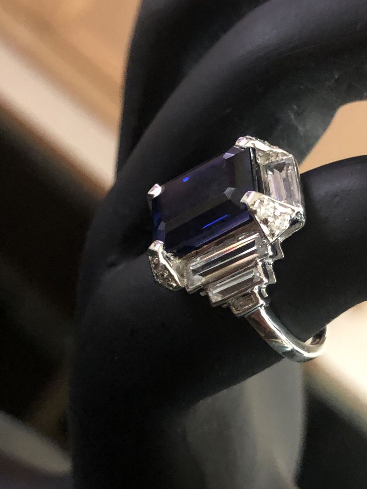 an emerald and diamond ring sitting on top of a black piece of cloth in front of a window