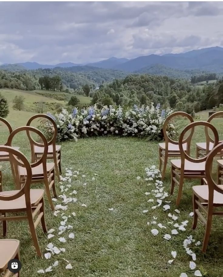 there are many chairs set up in the grass for an outdoor ceremony with white flowers on them