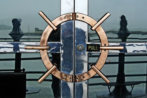 an image of a door that is reflecting the water and people in the reflection behind it