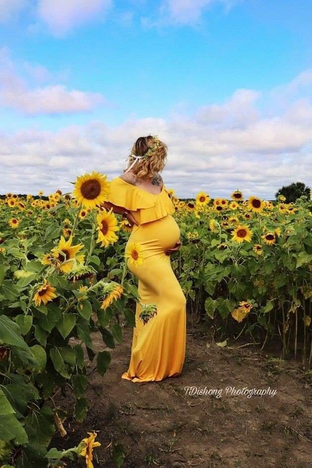 a pregnant woman in a yellow dress standing in a sunflower field with her back to the camera