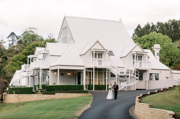 a bride and groom walking down the road in front of a large white house with stairs leading up to it