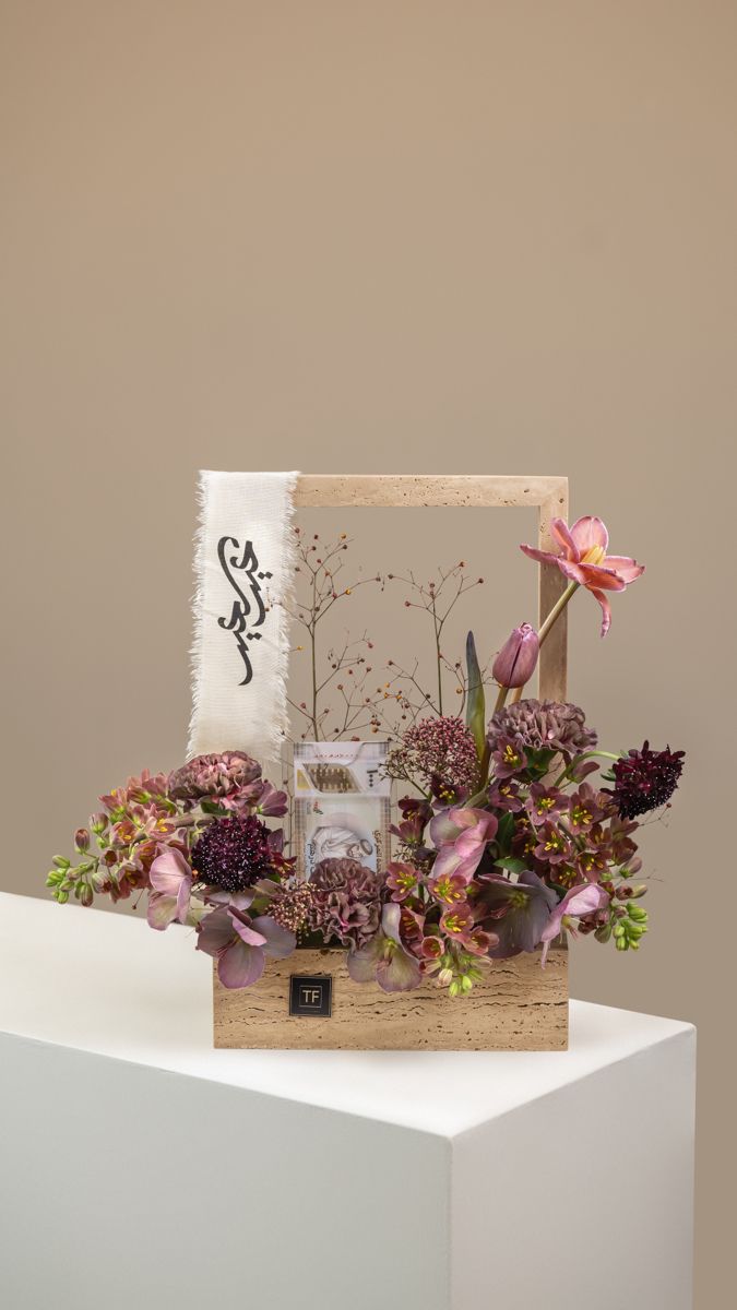 an arrangement of flowers in a wooden box on top of a white pedestal with a sign