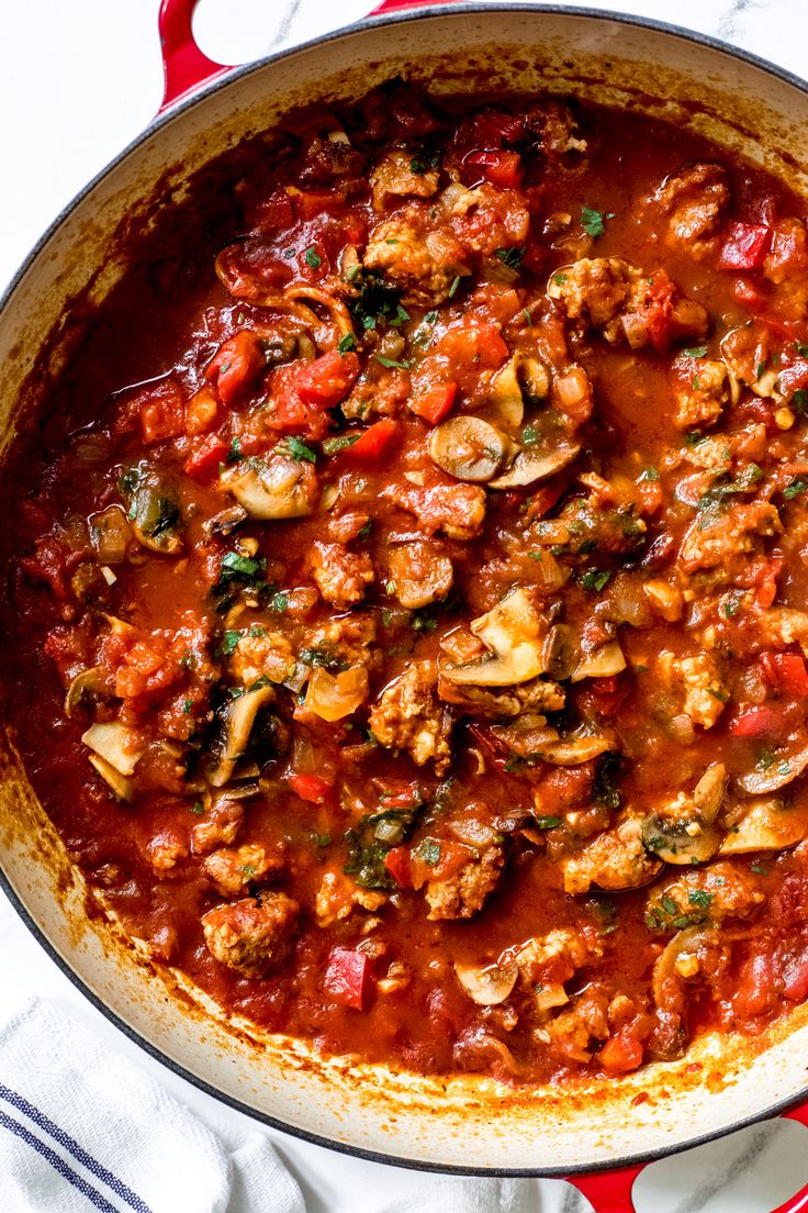 a pan filled with meat and vegetables on top of a white table cloth next to a red towel