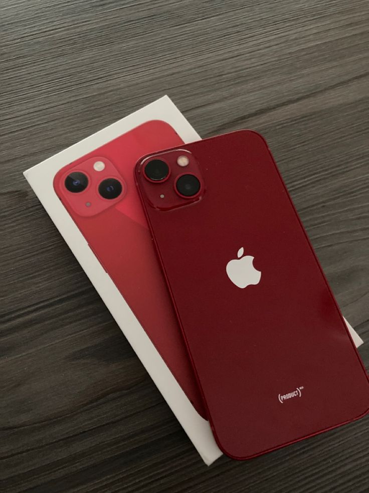 two red iphones sitting next to each other on top of a wooden table in front of a white envelope