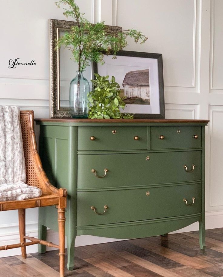 a green dresser sitting next to a chair with a plant on top and a framed photograph above it